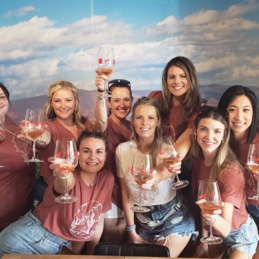 A group of women holding wine glasses in front of a sky background.