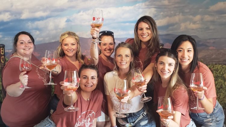 A group of women holding wine glasses in front of a sky background.